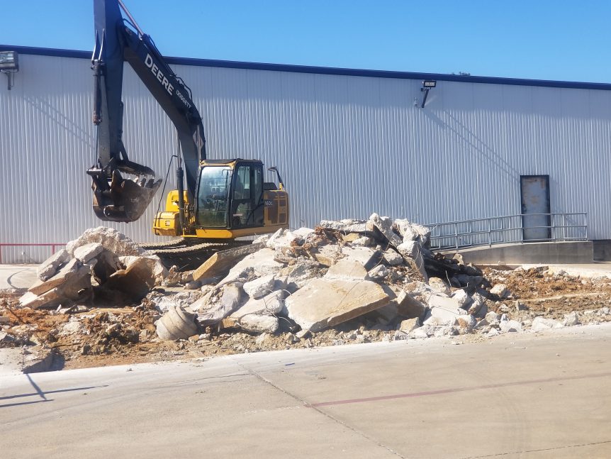An excavator breaks up concrete to begin demolition.